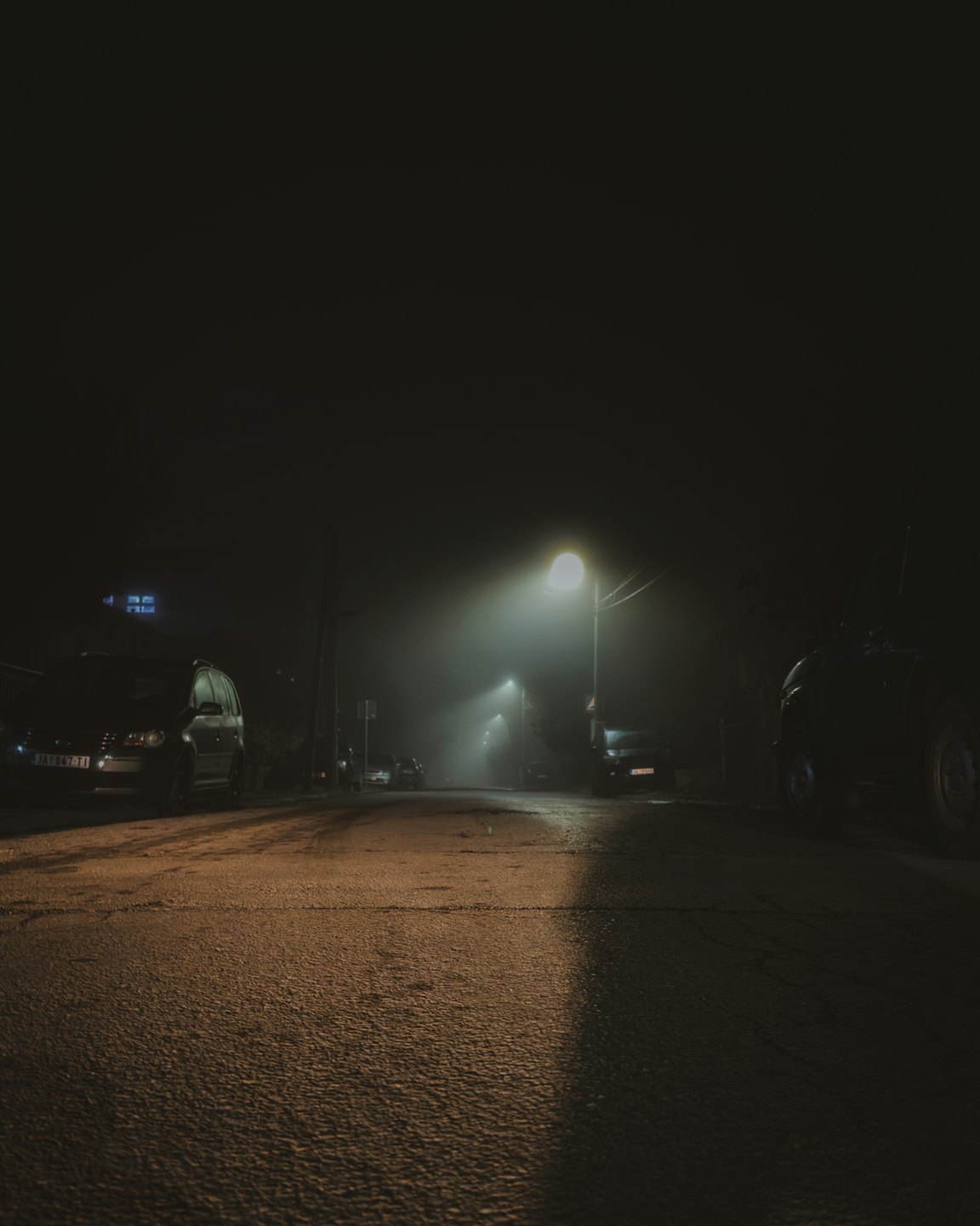 Cars parked along a wet misty street under a streetlight.